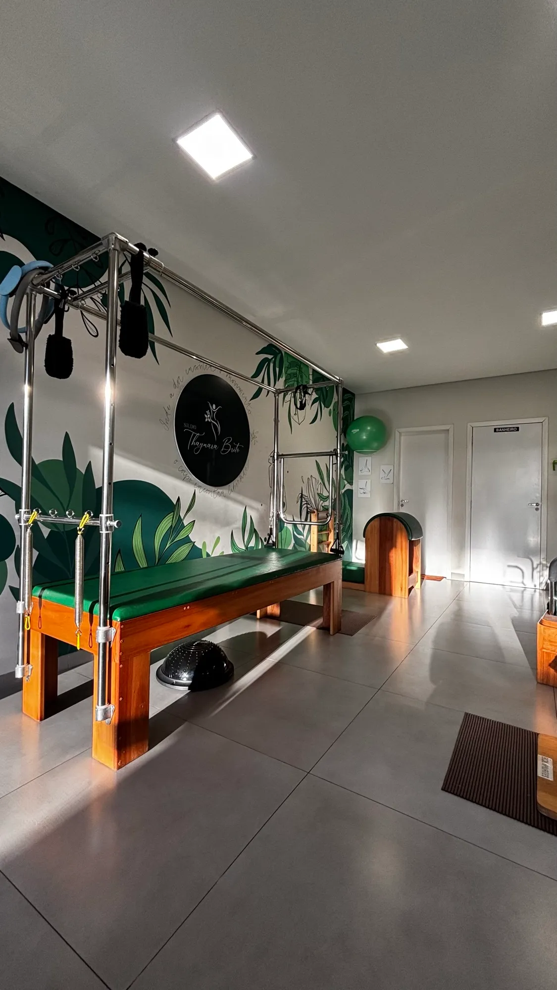 Sala do studio com o Cadillac de Pilates, a parede de folhagens verdes e o logo Studio Thaynara Brito